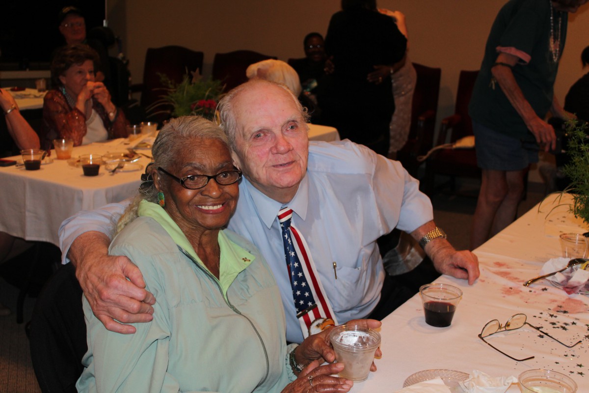 An elderly couple smiling and posing together at a social gathering.