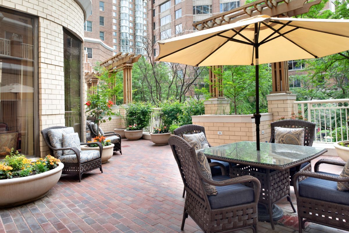A cozy outdoor patio with comfortable furniture and a large umbrella amidst an urban backdrop.