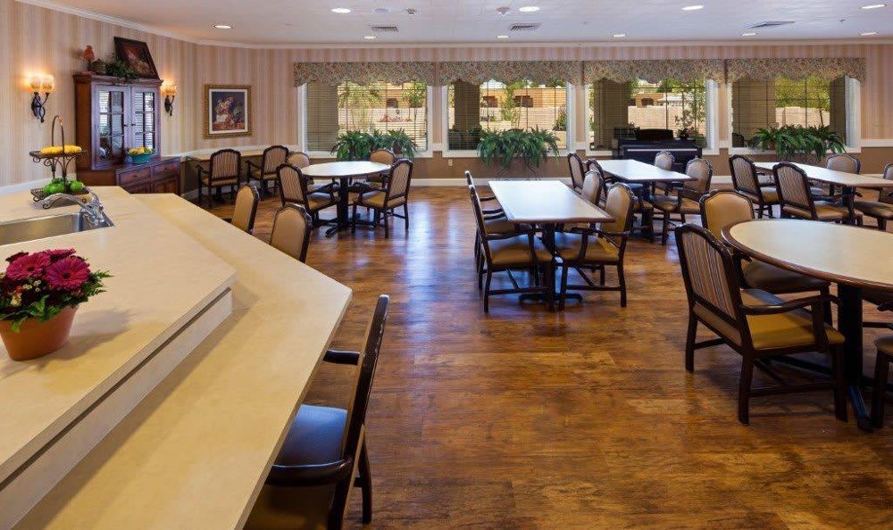A spacious dining area with several tables and chairs, featuring large windows and a wooden floor.