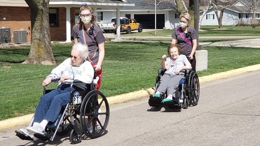 Caregivers assisting elderly individuals in wheelchairs during an outdoor walk.