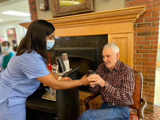 A caregiver assists an elderly man in a warm, indoor setting.