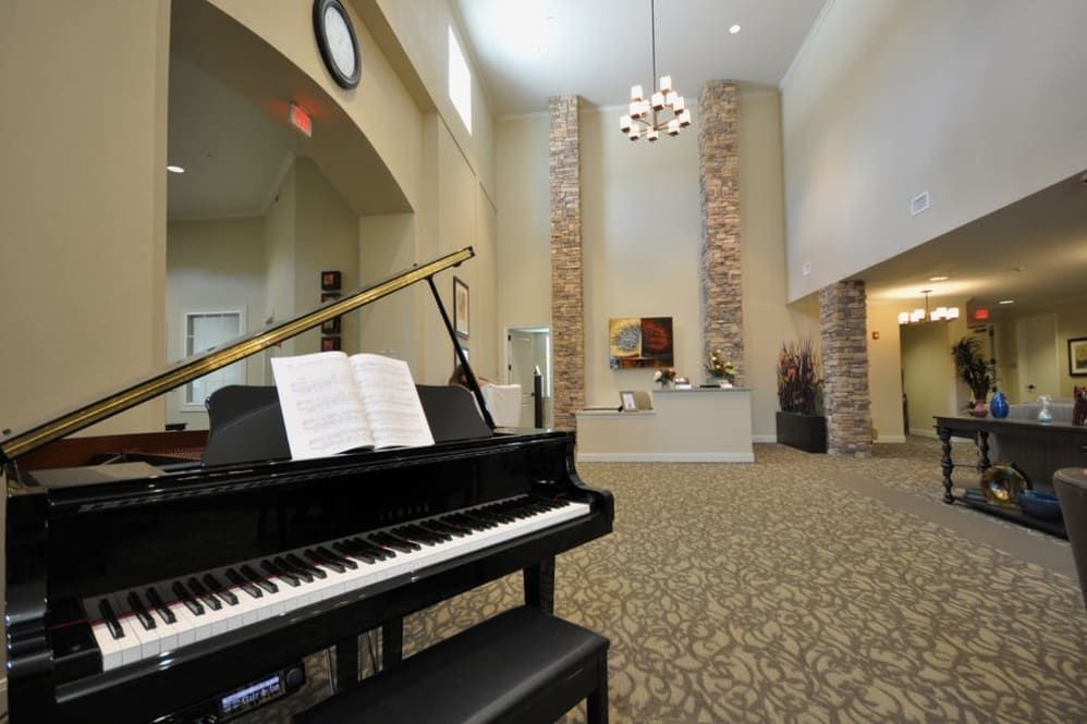 A spacious lobby featuring a grand piano under a chandelier and high ceilings.