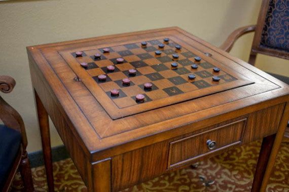 A wooden table with a checkerboard setup for playing checkers.