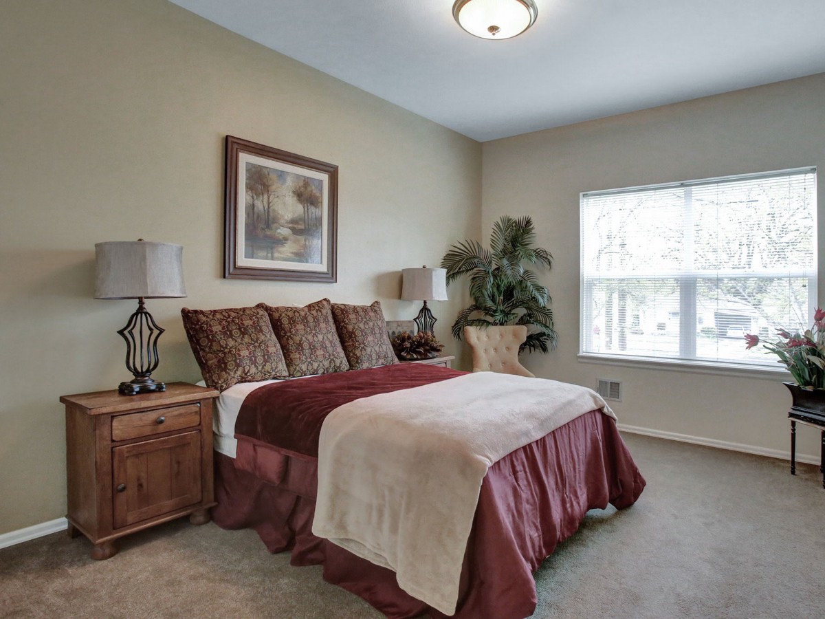 A cozy bedroom with a plush bed, decorative pillows, and a large window allowing natural light to fill the space.