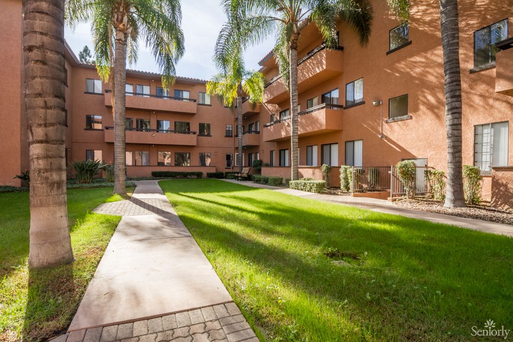 A serene courtyard surrounded by an apartment complex with lush green lawns and palm trees.