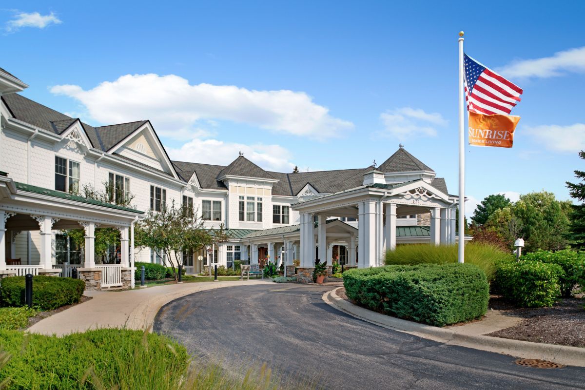 A large residential building with a prominent entrance and well-maintained landscaping, featuring an American flag.