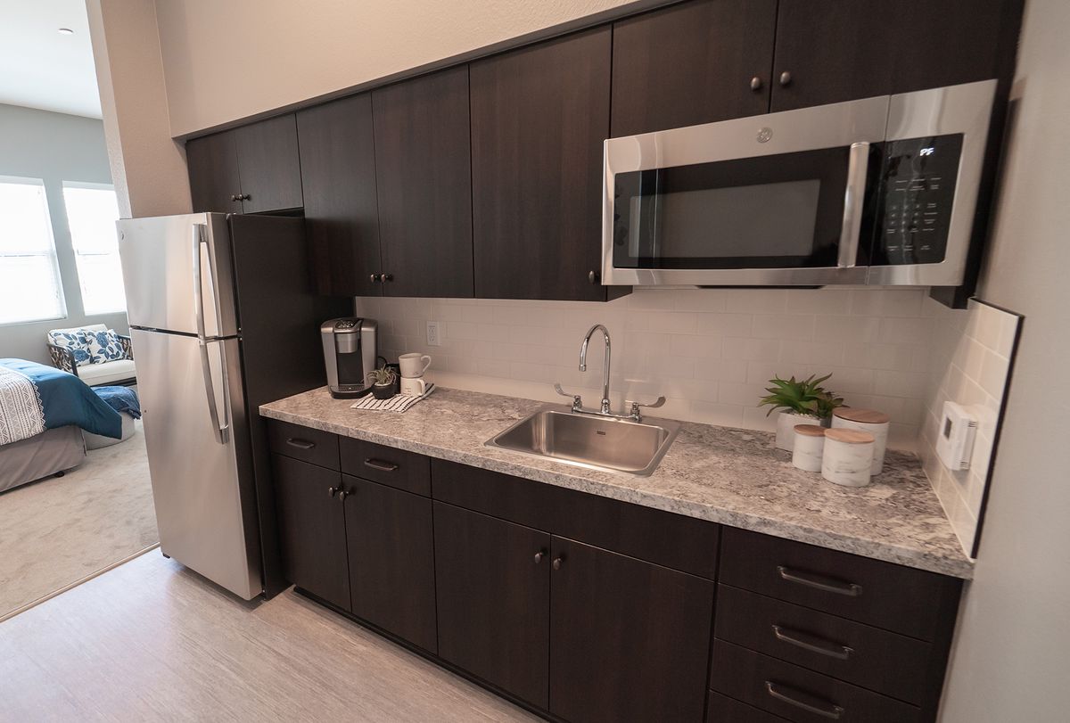 A modern kitchen with dark cabinetry, a stainless steel refrigerator, and a microwave.