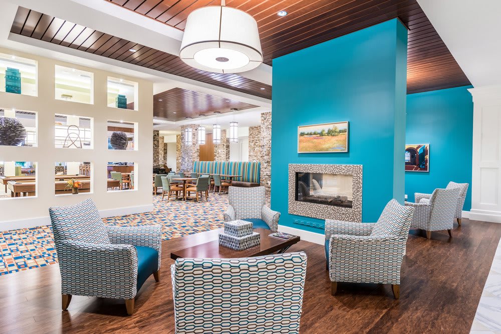 A modern living room with a blue accent wall and a cozy fireplace, featuring upholstered chairs and stylish decor.