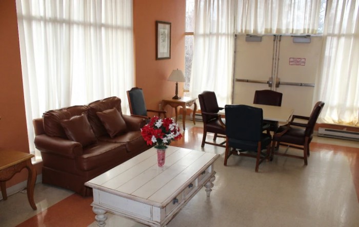 A cozy living room with a leather sofa, coffee table, and chairs, softly lit by natural light through the curtains.