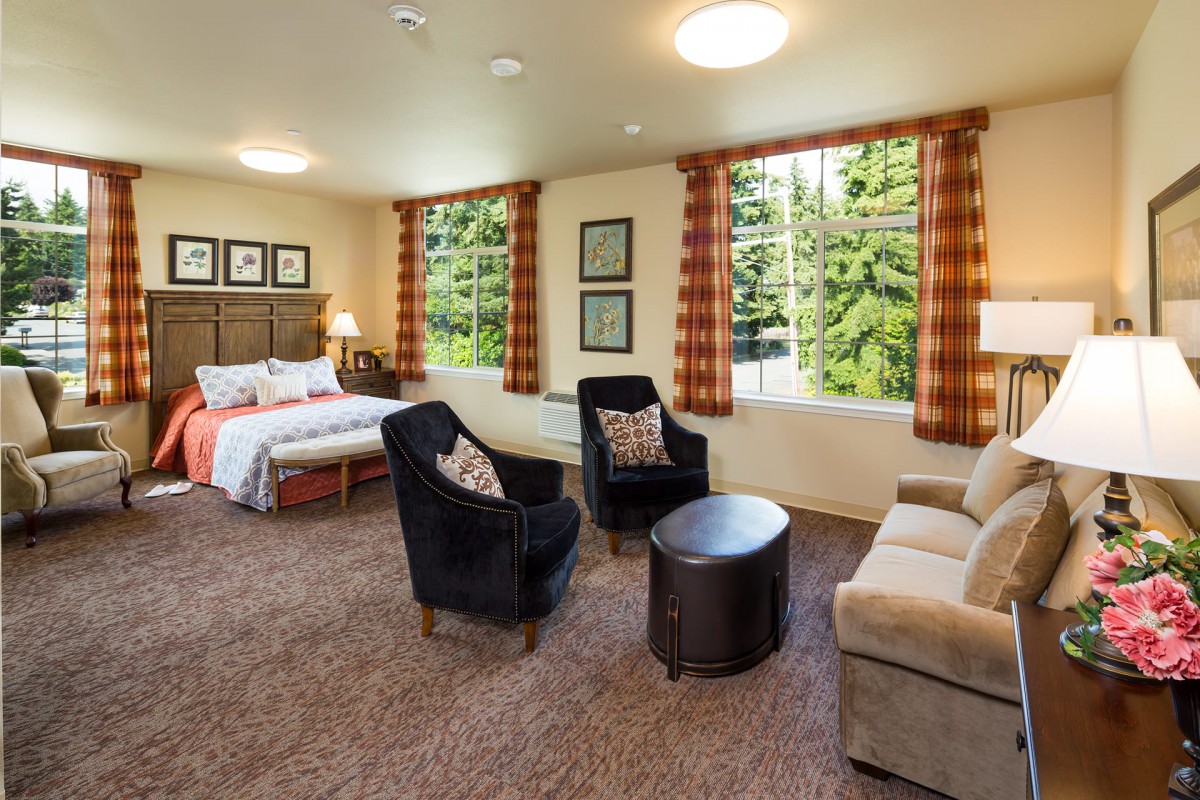 A cozy bedroom with a seating area featuring two chairs, a couch, and large windows offering a scenic view.