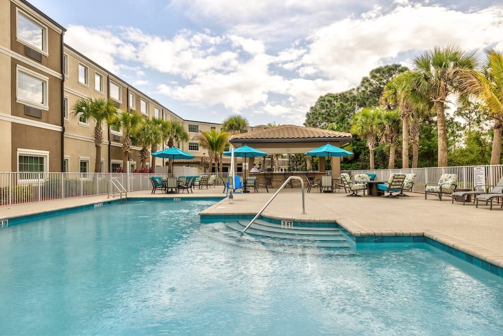 A sunny day at a resort with an inviting outdoor pool surrounded by palm trees, deck chairs, and patio umbrellas.