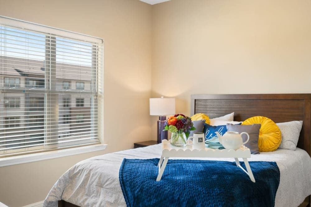 A cozy bedroom with a neatly made bed, featuring a decorative tray with flowers and tea set, illuminated by a bedside lamp.