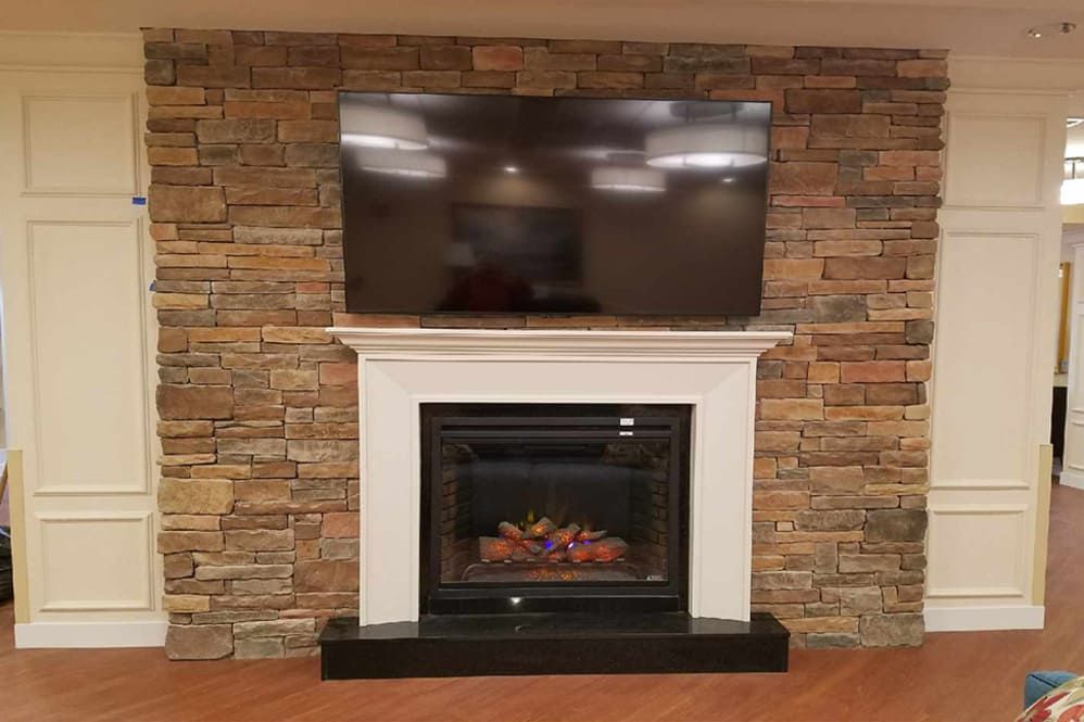 A cozy living room setup featuring a fireplace with a mounted television above it, set against a stone accent wall.