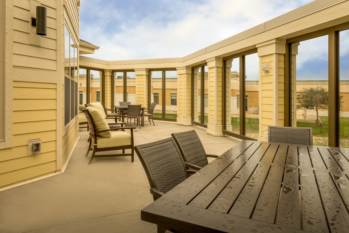 A spacious patio with outdoor seating and tables, surrounded by large windows on a sunny day.
