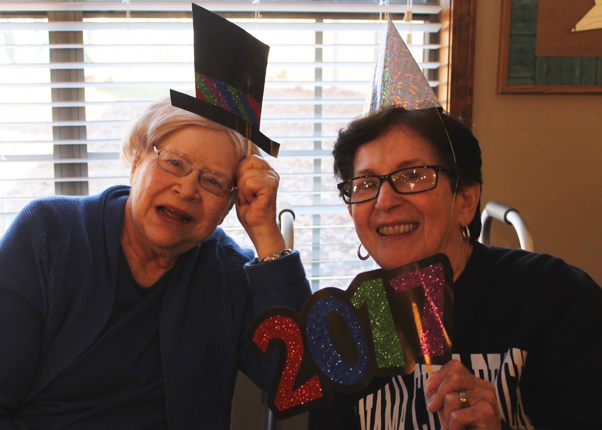 Two friends celebrating indoors with party hats and a '2021' sign.