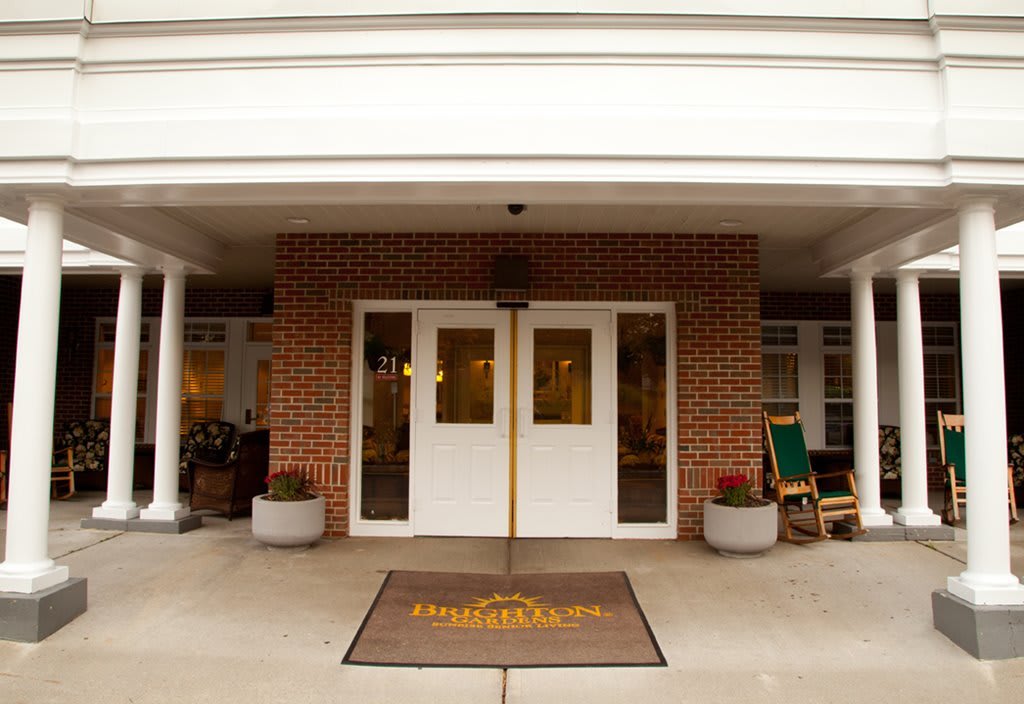 The main entrance of a building features double doors with a welcome mat and rocking chairs on either side.