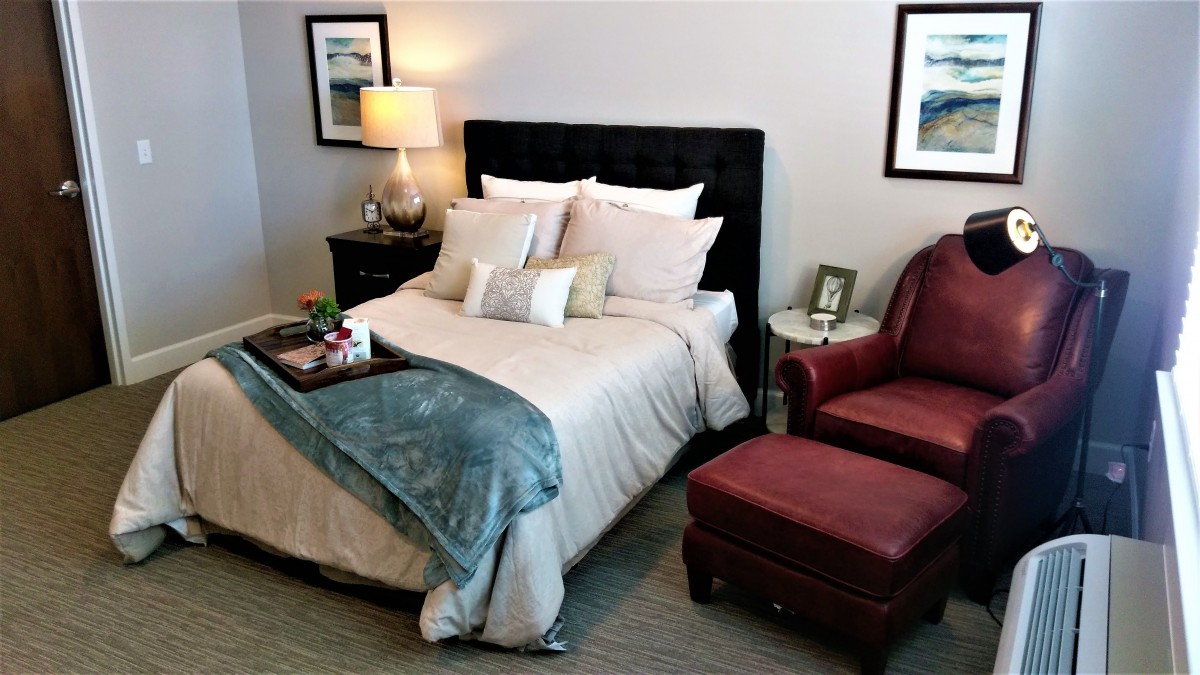 A cozy bedroom with a neatly made bed, inviting armchair, and warm lighting.