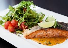 A gourmet dish featuring grilled salmon with a side of arugula and cherry tomato salad, garnished with lime.