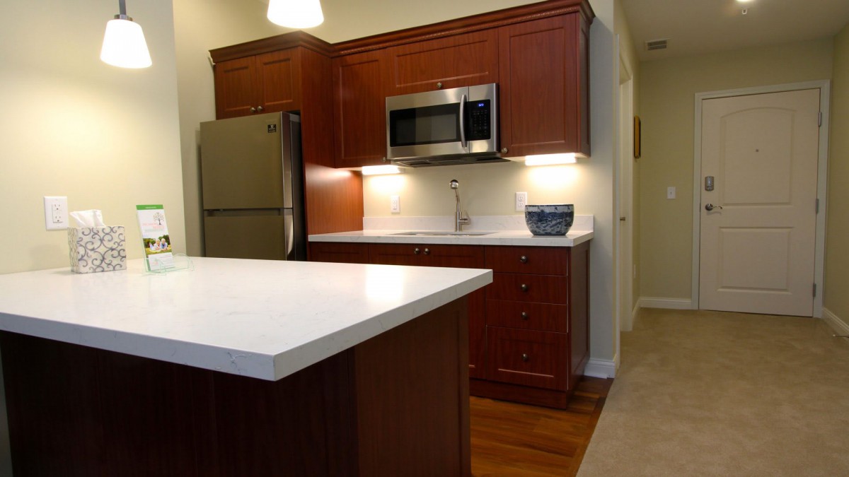 A modern kitchen with wooden cabinets, a stainless steel microwave, and a large countertop.