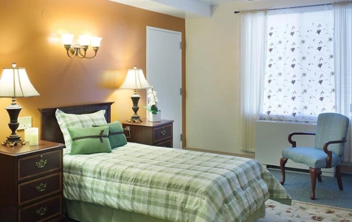 Cozy bedroom with a single bed, bedside lamp, and window with patterned curtains.
