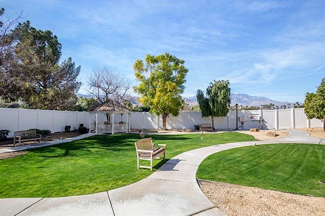 A well-maintained backyard featuring a grassy area, trees, and a curved pathway leading to a bench.