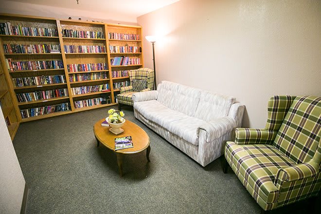 A cozy living room with a bookshelf, sofa, and chairs surrounding a coffee table.