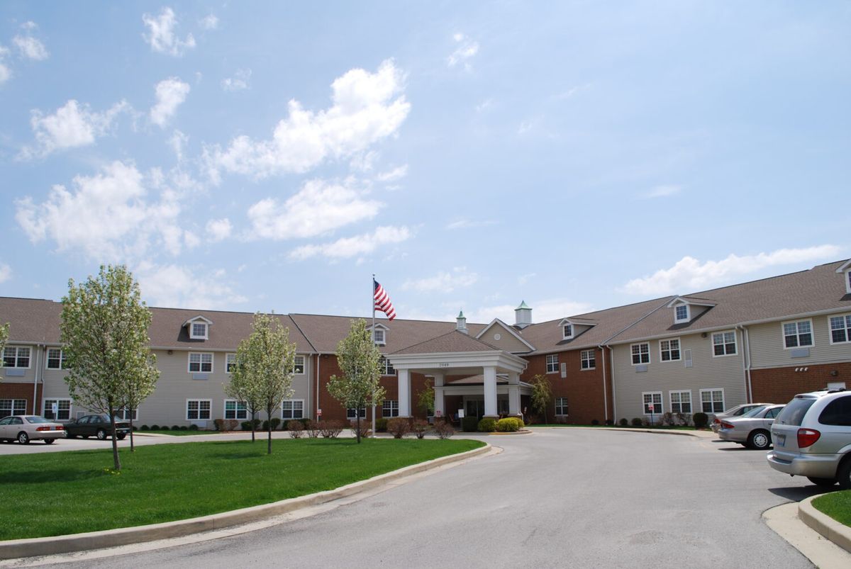 A large building with an entrance, surrounded by a parking lot and green lawn under a partly cloudy sky.