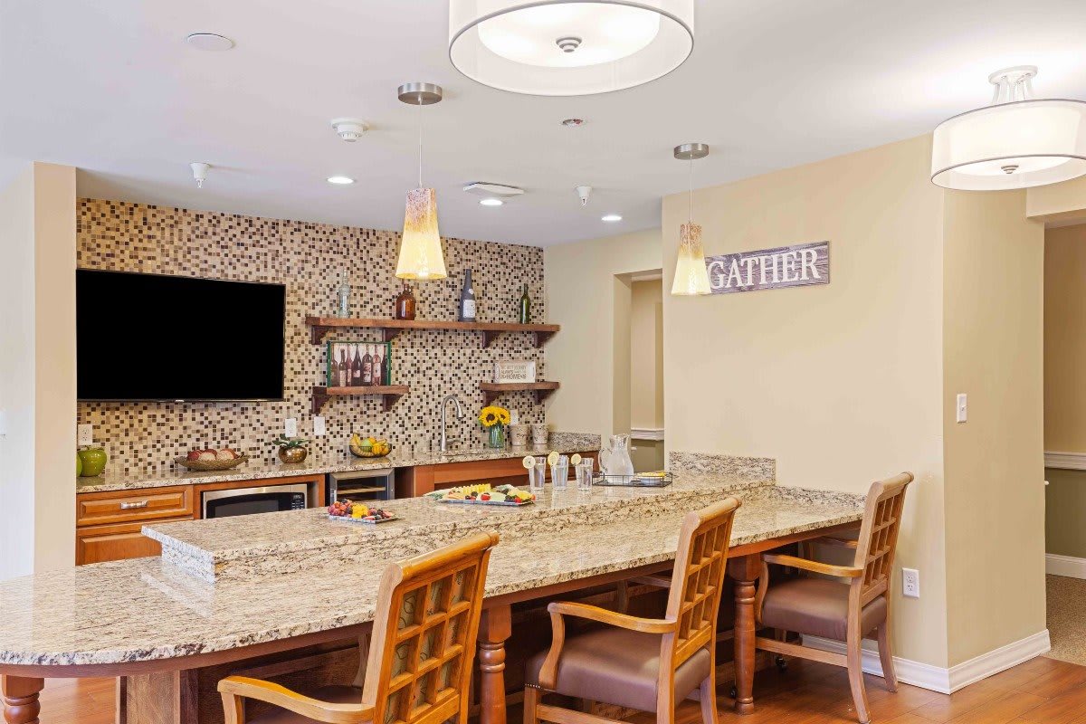 A modern kitchen interior with a spacious countertop and wooden chairs, featuring decorative shelves and stylish lighting.
