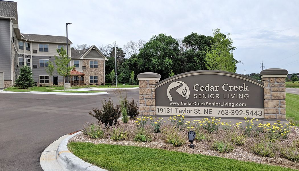 Entrance sign to Cedar Creek Senior Living with a landscaped area and building in the background.