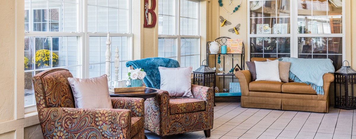 A cozy living room filled with patterned armchairs, decorative plants, and warm natural lighting.