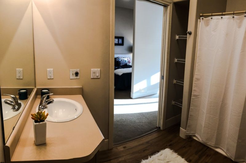 A bathroom with a view into a bedroom, featuring a sink and mirror.