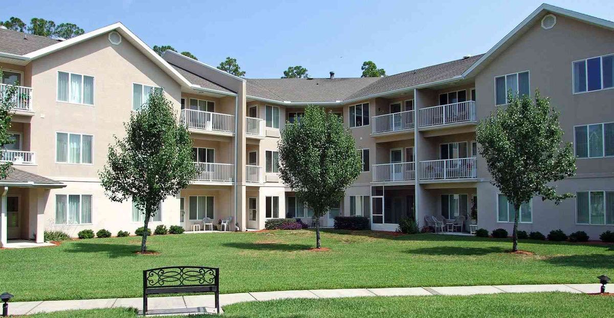 A multi-story apartment building with balconies and a well-maintained lawn featuring a park bench.