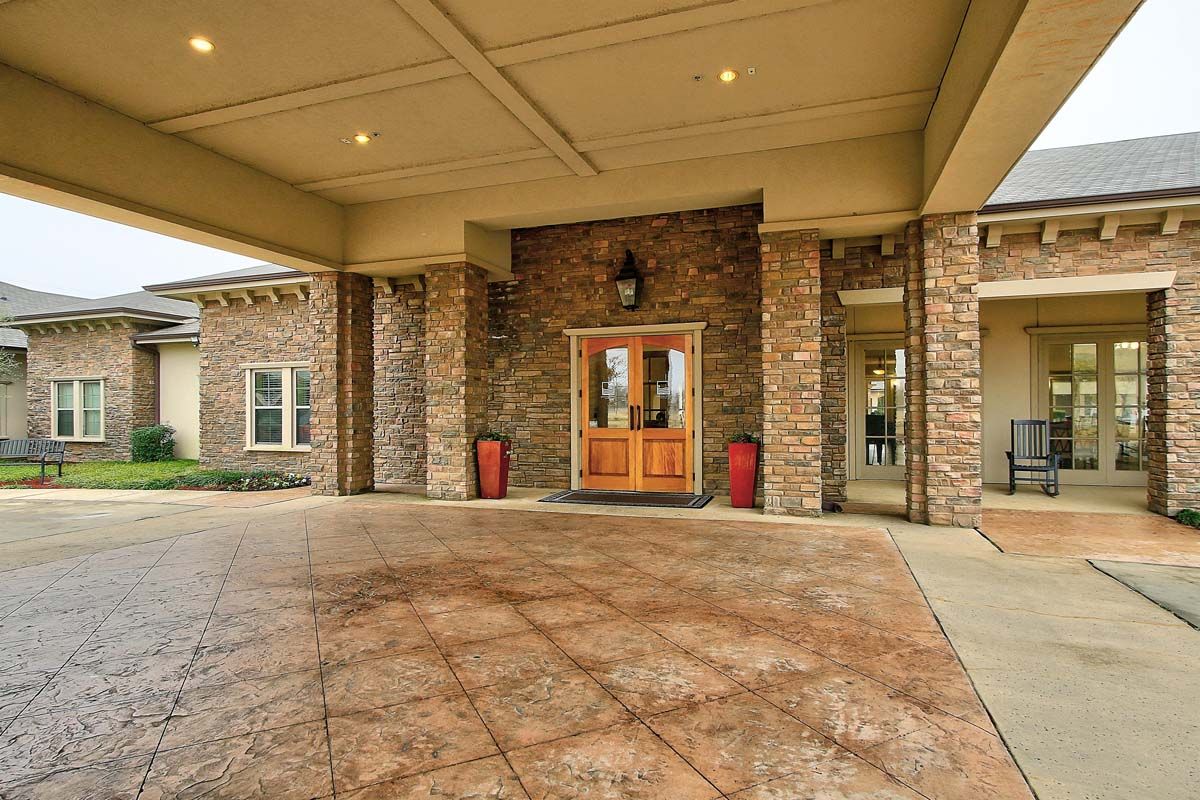 The image shows a building entrance with a stone facade and wooden doors, featuring a covered entryway.