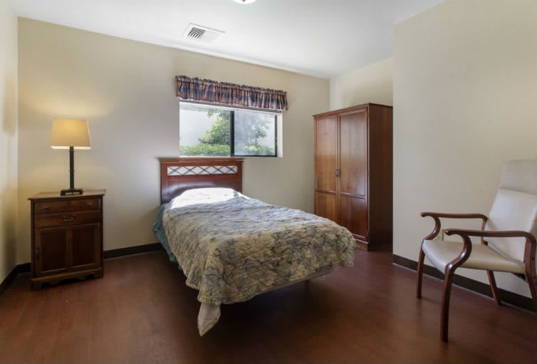 A simple bedroom with a single bed, wardrobe, lamp, and chair.