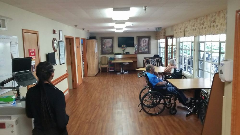 Interior of a nursing home with residents in wheelchairs and tables.