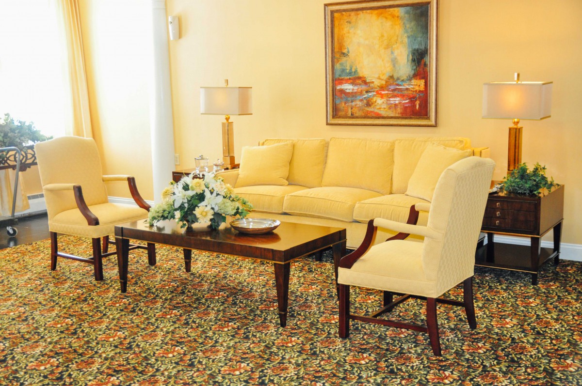 A cozy living room with a yellow sofa and armchairs, complemented by a wooden coffee table and floral decor.
