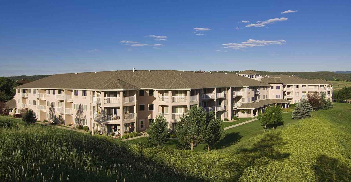 A scenic view of a residential apartment building surrounded by lush greenery and under a clear blue sky.