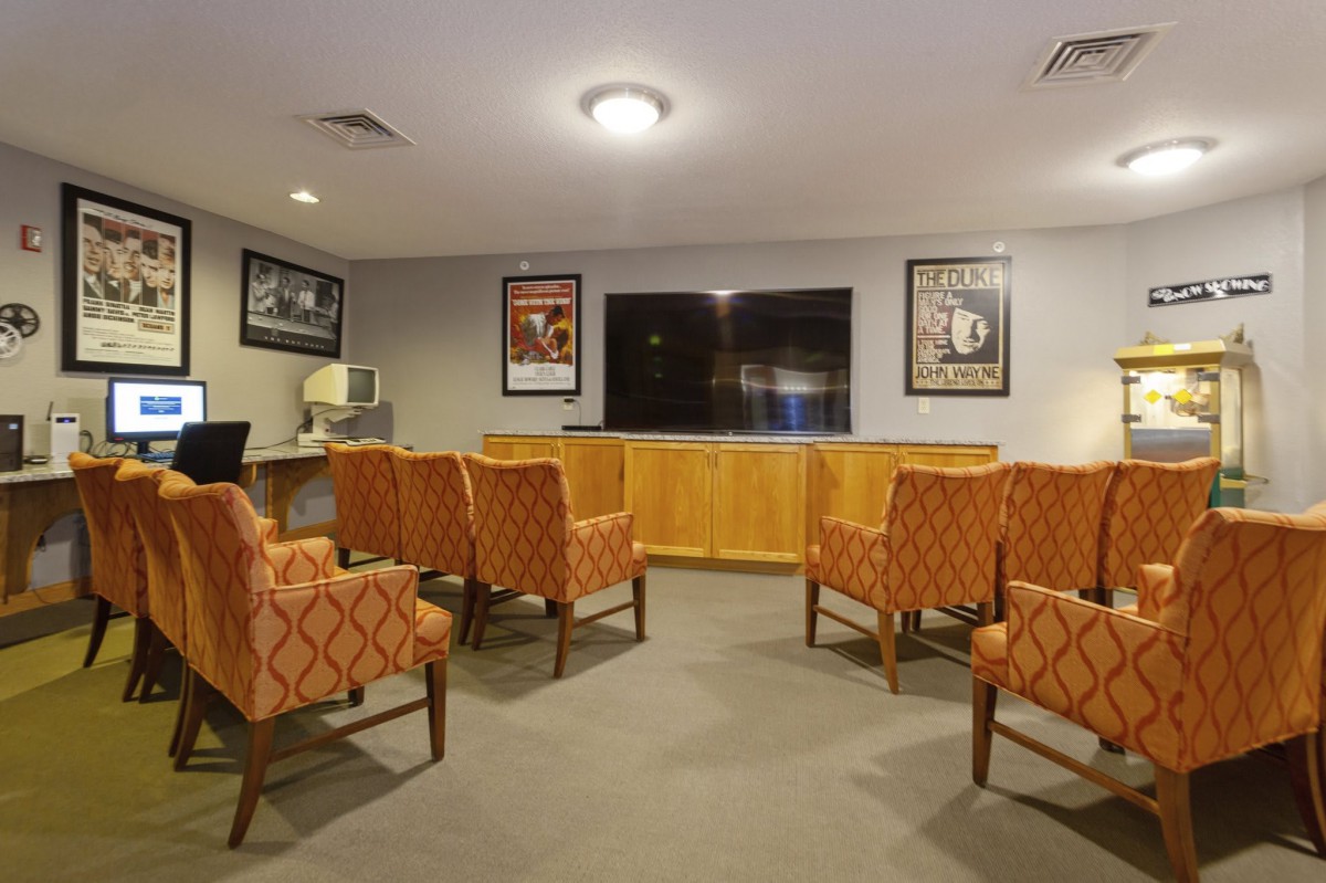 A cozy seating area with orange-patterned chairs facing a large television, adorned with film posters on the walls.
