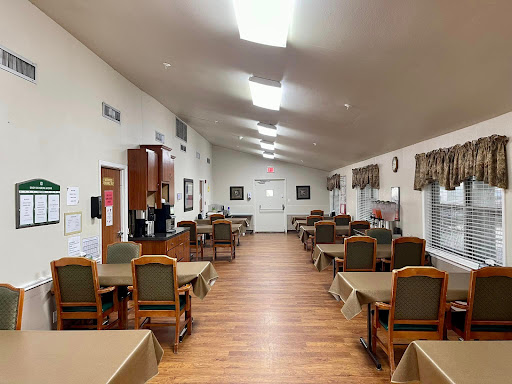 A spacious dining area featuring neatly arranged tables and chairs, illuminated by bright overhead lights.