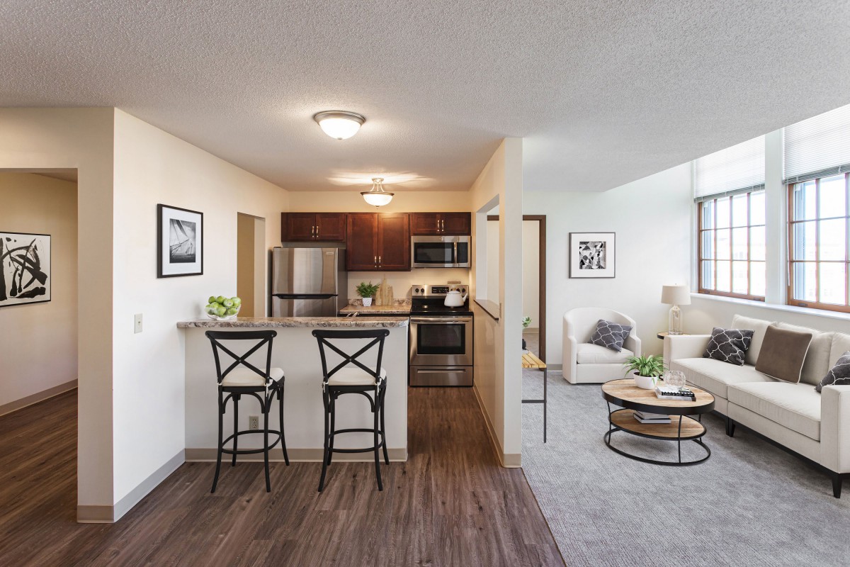 A modern apartment interior featuring an open floor plan with a kitchen and living room area, highlighted by stainless steel appliances and stylish bar stools.