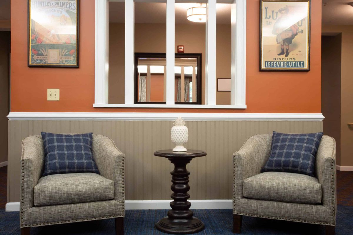 A cozy waiting room with two armchairs and a small table topped with a lamp, surrounded by decorative artwork.