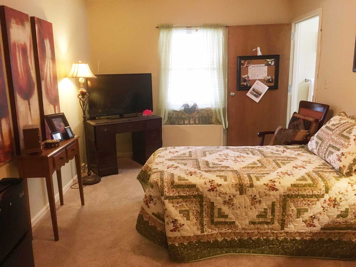 A cozy bedroom with a quilted bedspread, television, and warm lighting.