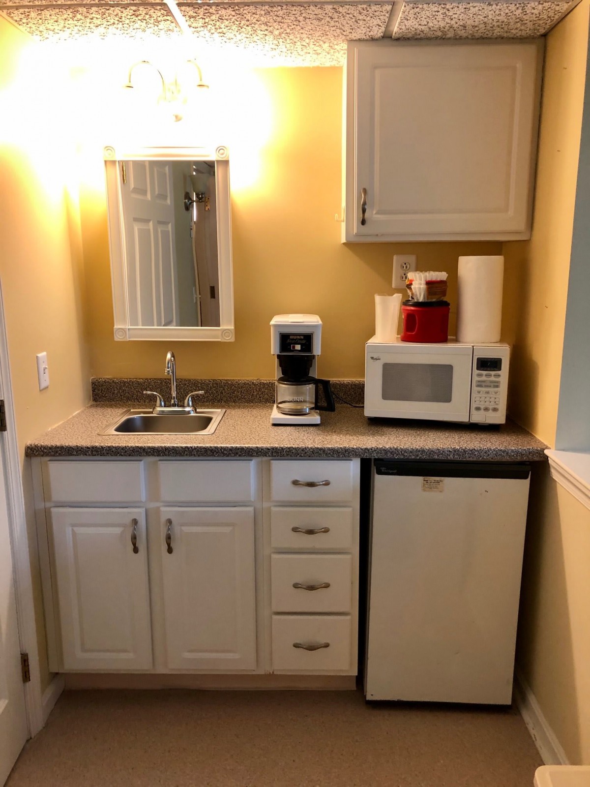 A compact kitchenette with a microwave, coffee maker, mini fridge, and sink.
