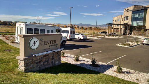 A view of the parking area and entrance sign for a center, with a bus and cars parked in the foreground.