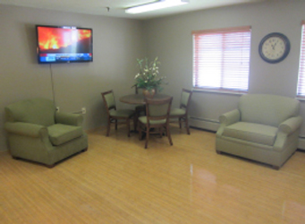 A cozy sitting area featuring comfortable green chairs, a dining table with chairs, and a television.