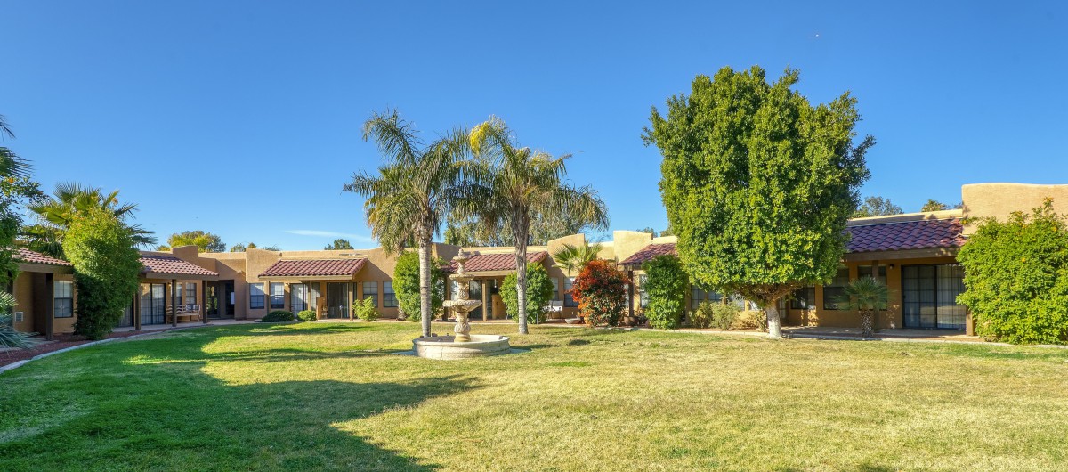 A beautiful house with a landscaped garden featuring palm trees and a fountain on a sunny day.