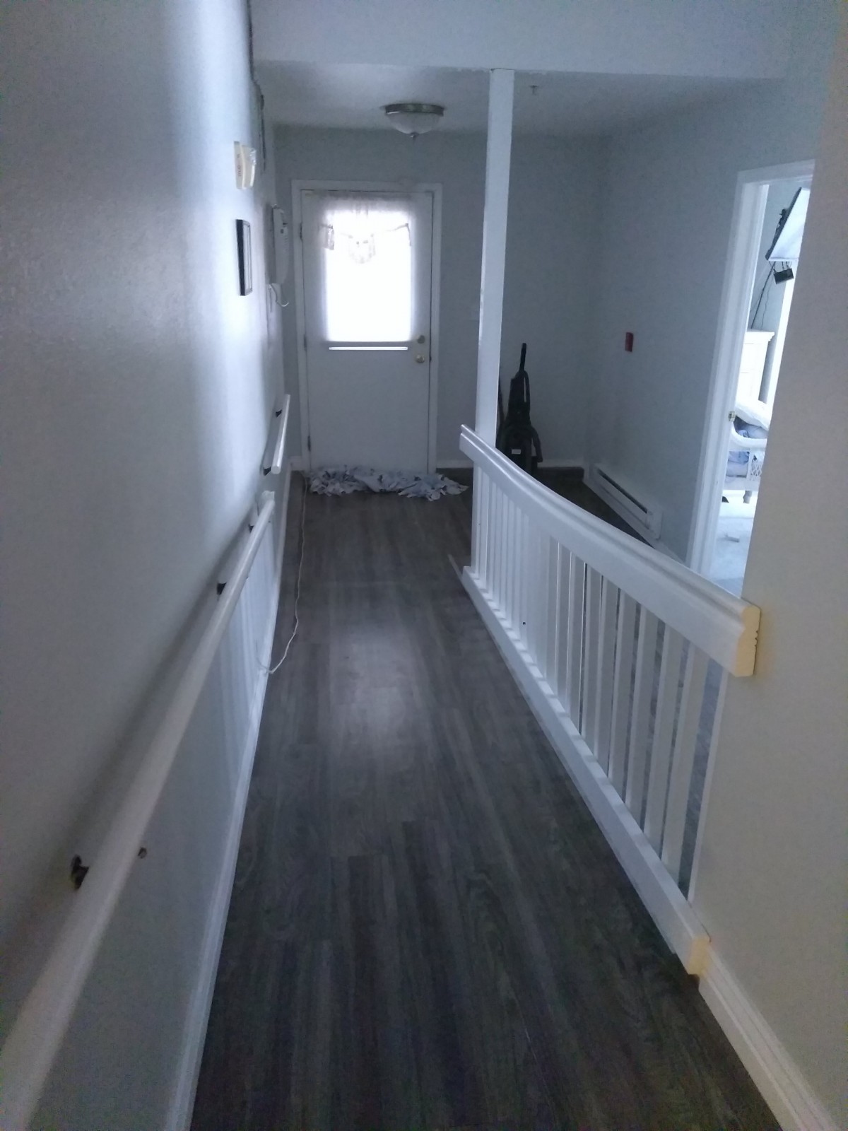 A hallway with handrails, leading to a door and overlooking stairs.