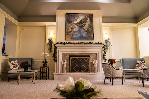 A cozy and elegantly decorated living room featuring a classic fireplace, beautiful artwork, and festive floral arrangements.