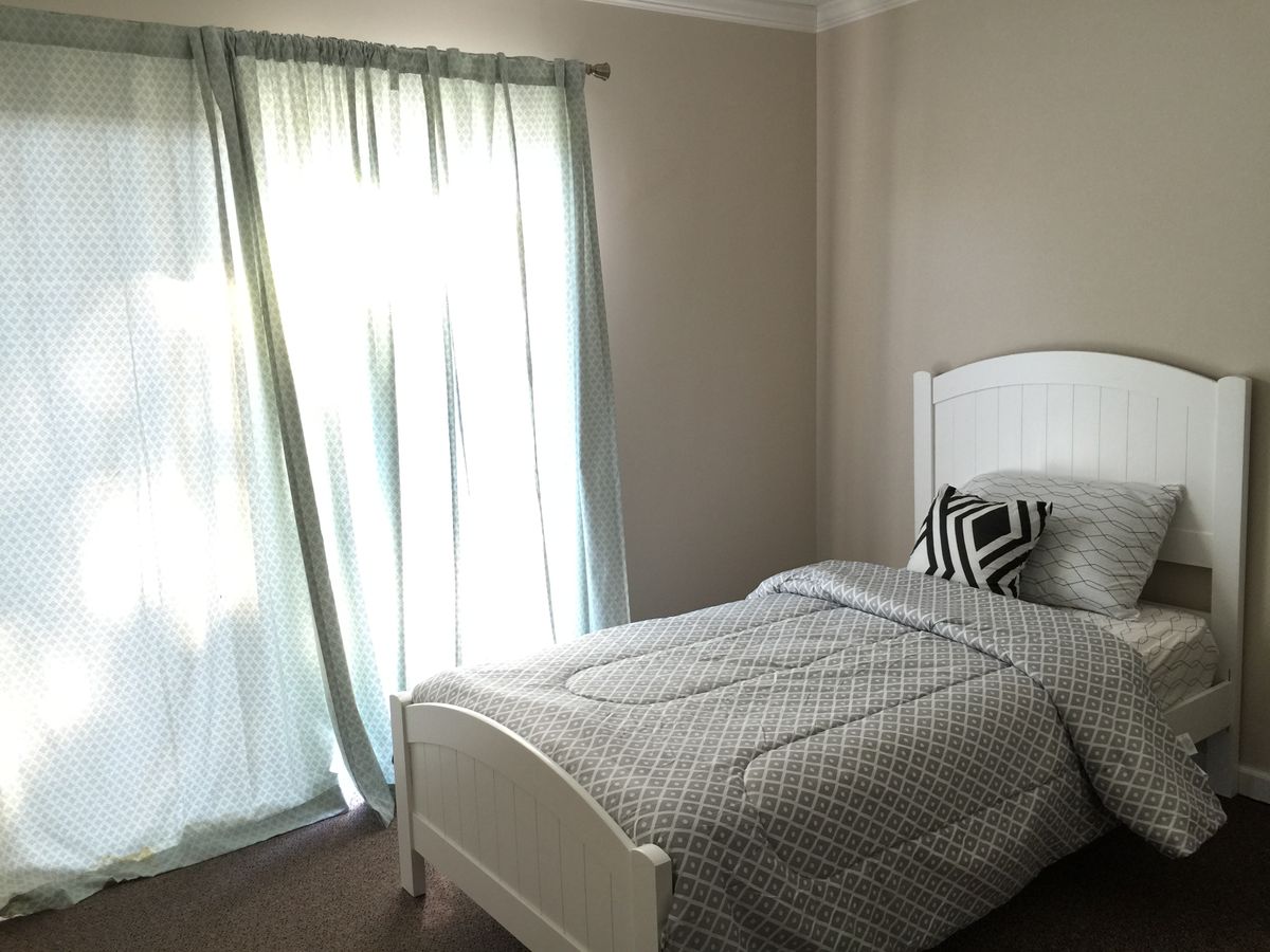 A minimalist bedroom with a single bed and soft curtains allowing natural light in.