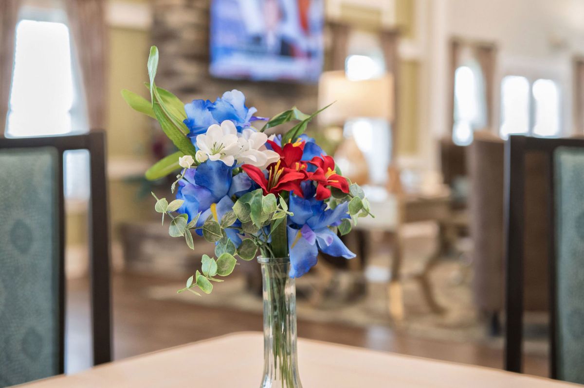 A colorful bouquet of flowers in a vase set against a blurred interior background.